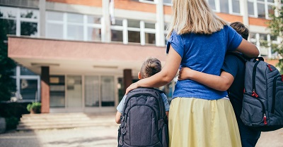 una mamma di spalle accompagna due figli a scuola